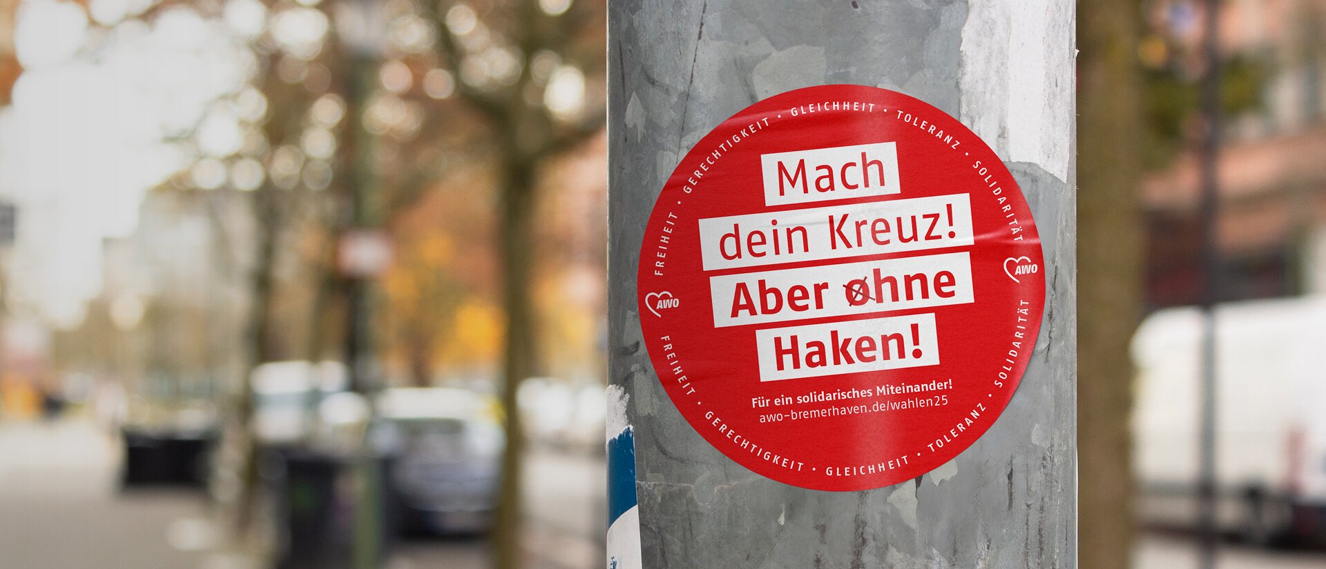 Das Foto zeigt einen Aufkleber, der auf einer Straßenlaterne geklebt wurde. Auf dem Aufkleber steht: Mach Dein Kreuz! Aber ohne Haken